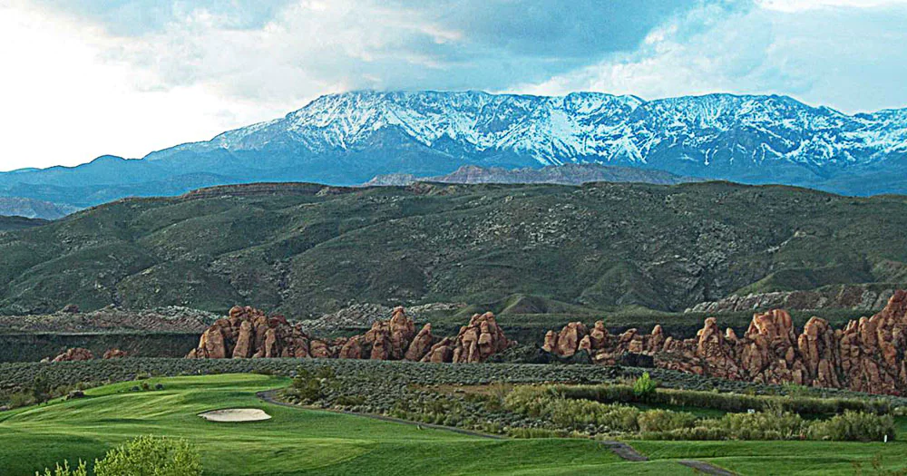 Scenic view of Hurricane, Utah with snow capped mountains in the distance and red rock and a green gold course in the foreground.