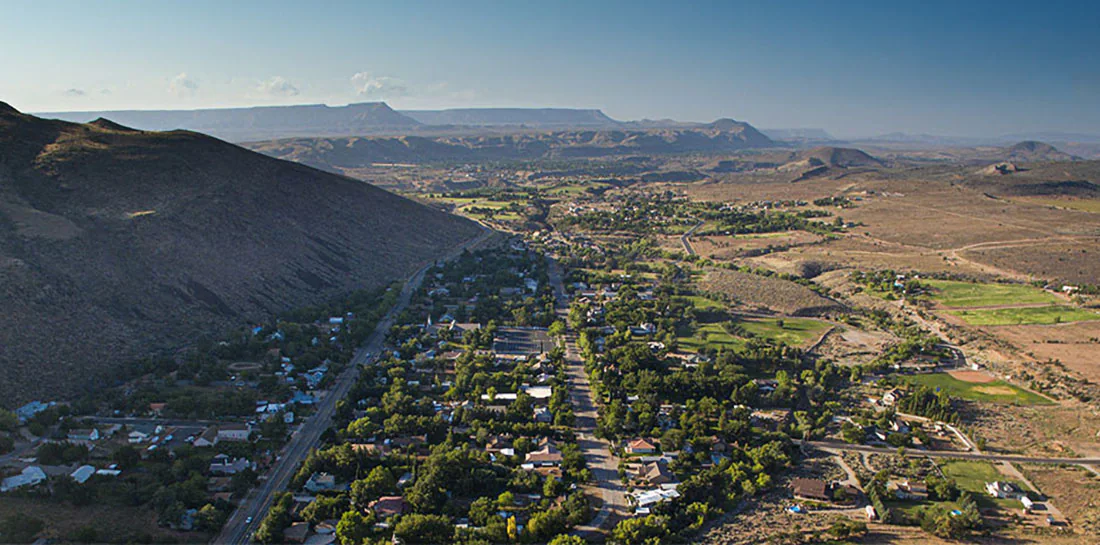 A view from above of Toquerville, UT. A small town at the base of steep hill that shadows part of the town.