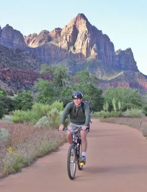 Man cycling on dirt path with mountains in view