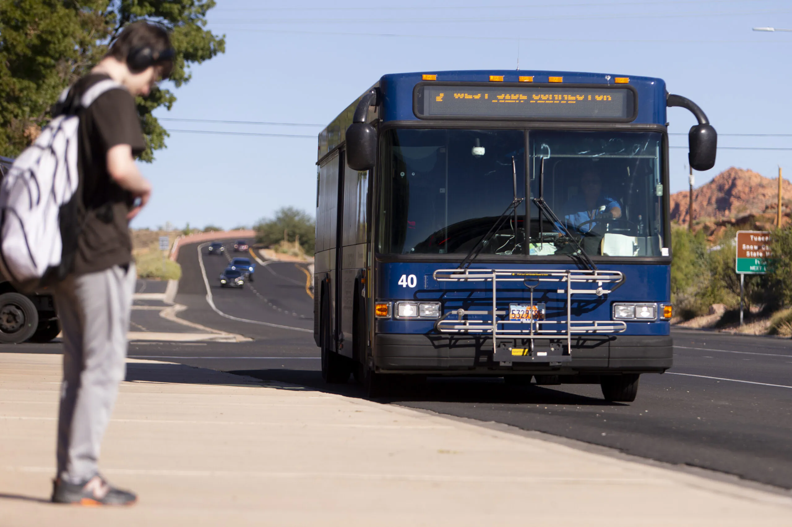 Blue bus (40) displaying "West I. Jacob's Hill I. Way", person with backpack and headphones walking