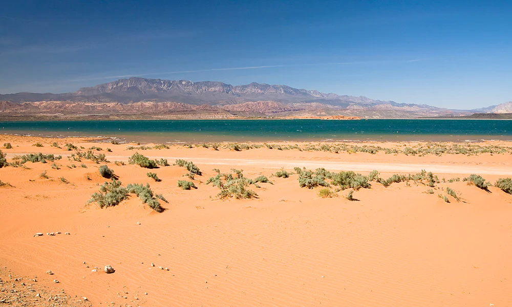 Desert sand, bushes, blue lake, and distant mountains