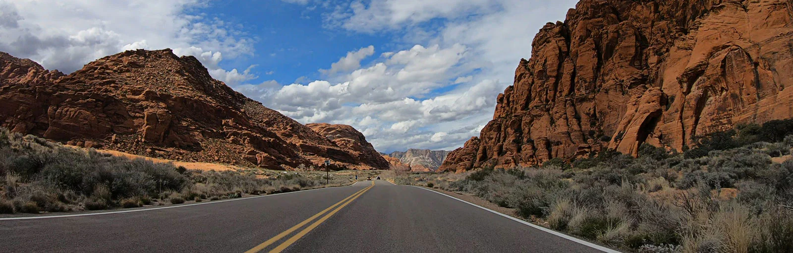 Asphalt road with yellow center lines flanked by red rock cliffs and desert vegetation