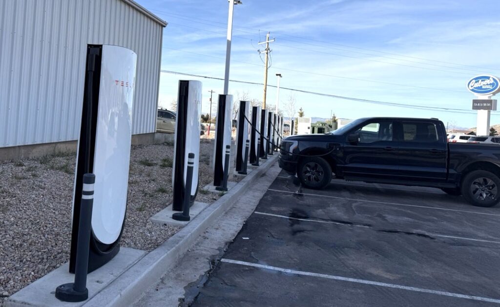 A dark colored Ford 150 Lightning is charging at a Tesla Supercharger in Cedar City.