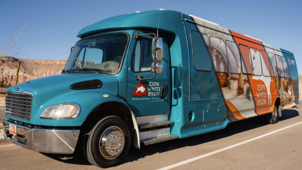 Zion White Bison shuttle is parked along the side of a road and features White Bison-branded graphics along the side and door.